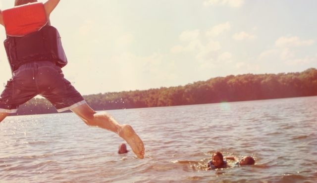 photo of boy jumping in a lake