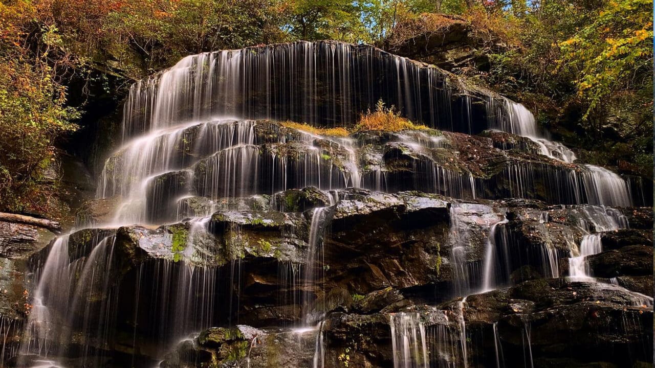 Waterfall cascading over rocky ledges surrounded by vibrant fall color in Oconee County, ideal for a fall hike.